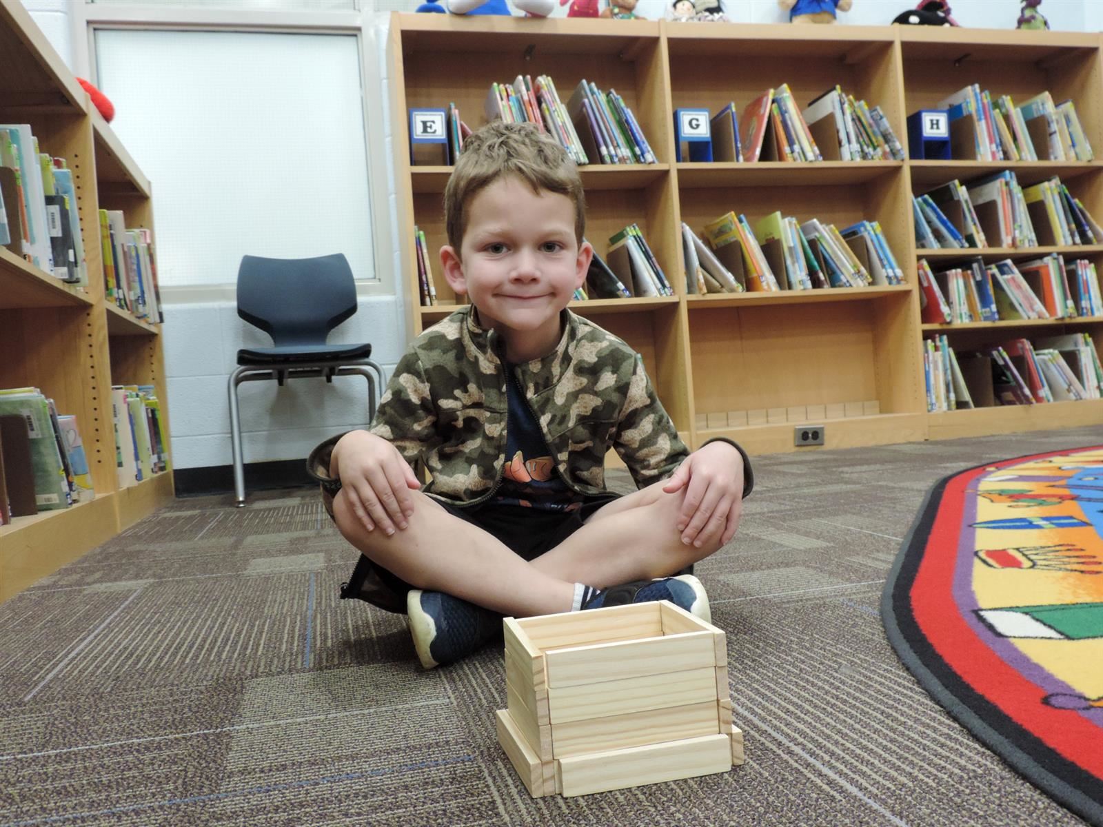 Boy in camo smiling while building a wooden library